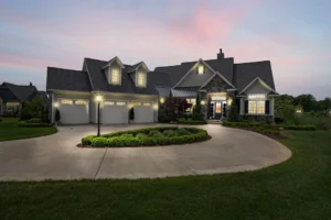 Two-story home with a shingle roof lit up at dusk