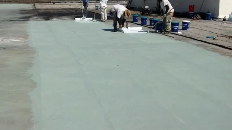Crew applying base coat with embedded reinforcing fabric on a concrete roof deck