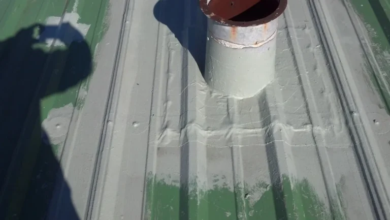 Pipe penetration on a metal roof sealed with base coat and reinforcing fabric